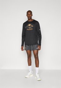 Black long-sleeve shirt with orange mountain graphic and gray shorts featuring a textured pattern. White athletic socks and shoes complete the outfit.
