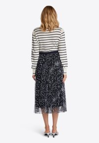 Randig långärmad topp i kräm och marinblå, ihop med en genomskinlig svart kjol med ett mönster som liknar vita fjädrar. Platta vita klackskor.