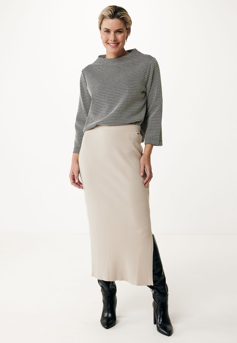 Gråmönstrad topp med hög krage, beige ribbad midikjol och svarta knähöga stövlar. Släta texturer med en åtsittande siluett.