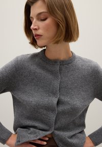 Cardigan in lana grigia con collo rotondo, sei bottoni frontali, polsini a costine e una trama discreta. Vestibilità slim con un design pulito e minimalista.