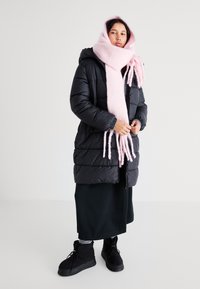 Czarna kurtka puchowa z kapturem, różowy wełniany szalik, długa czarna spódnica i czarne botki z teksturowaną podeszwą. Posiada elastyczne mankiety i zamek błyskawiczny.
