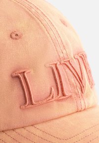 Roze katoenen baseballpet met geborduurde "LIVE" tekst, met een gestructureerde vorm, zichtbare stiksels en een textuurstof.