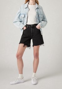 Chaqueta de mezclilla azul claro sobre una camiseta blanca, combinada con shorts de mezclilla negra de tiro alto con dobladillos desgastados. Zapatillas blancas completan el conjunto.