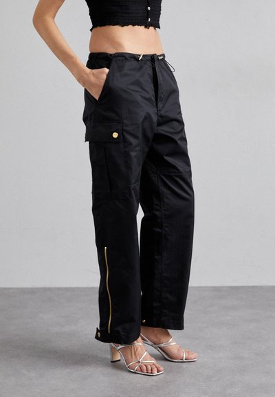 Pantaloni cargo negri cu accente din hardware auriu, având buzunare laterale, margini cu fermoar și o croială relaxată. Material neted cu un finisaj mat.