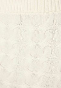 Knit sweater in off-white with a textured cable pattern and ribbed hem. Soft material enhances comfort and warmth.