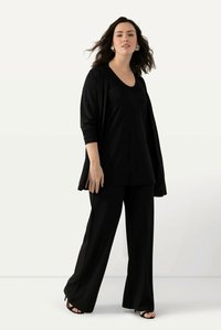 Svart lös passform topp med rundad halsringning, i kombination med vida svarta byxor. Outfiten har ett mjukt tyg och en avslappnad design. Svarta sandaler.