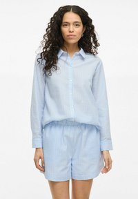 Light blue checkered button-up shirt with long sleeves, paired with matching light blue shorts. Both garments made from a smooth, lightweight fabric.