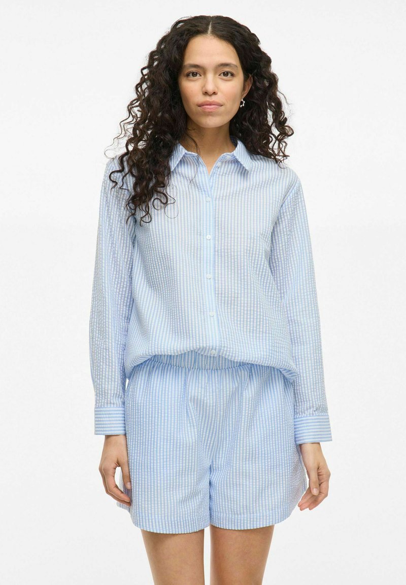 Light blue checkered button-up shirt with long sleeves, paired with matching light blue shorts. Both garments made from a smooth, lightweight fabric.