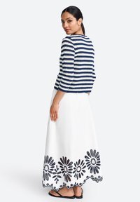 Navy and white striped knit jacket with three-quarter sleeves, paired with a white skirt featuring black floral embroidery at the hem.