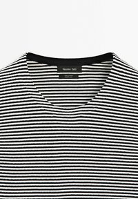 Top in cotone a righe con linee orizzontali nere e bianche, scollatura tonda e una consistenza liscia. Etichetta del marchio visibile all'interno.