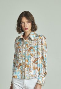 Blusa a maniche lunghe con un motivo astratto blu chiaro, bianco e marrone. Presenta un grande colletto e dettagli decorativi con bottoni.