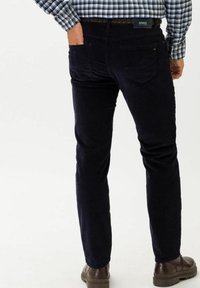 Marinblå kordflortbyxor med smal passform, som har två bakfickor, en subtil strukturerad mönster och bruna läderskor.