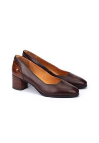 Une paire de chaussures à talons bas pour femmes en cuir brun foncé avec des orteils ronds et des accents texturés au talon, présentée sur un fond blanc.