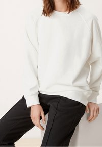 Felpa bianca a maniche lunghe con maniche raglan e colletto rotondo, abbinata a pantaloni neri. Tessuto liscio, vestibilità comoda.