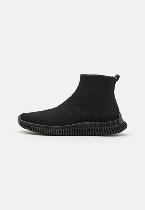 Sort slip-on sneakersstøvle med strækbar strikket overdel og tekstureret fleksibel sål på hvid baggrund.