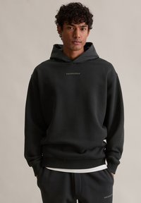 Czarny kapturowy sweatshirt z miękkiego materiału z prążkowanymi mankietami, z minimalistycznym logo na klatce piersiowej i pasującymi czarnymi spodniami.