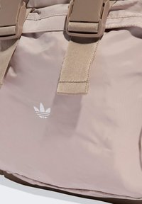 Svetloružová nylonová taška so dvoma béžovými prackami, s bielym logom Adidas. Textúrovaná látka s hladkým povrchom. Kompaktný obdĺžnikový tvar.