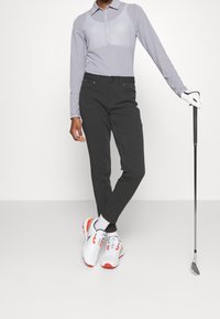 Långärmad, ljusblå och vit randig polo med knäppning, kombinerad med svarta byxor och vita golfskor med röda detaljer.