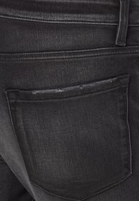 Czarne dżinsy z denimu z tylną kieszenią ozdobioną subtelnym przeszyciem. Tekstura jest gładka z delikatnym połyskiem.