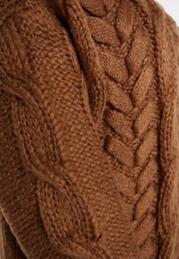 Brun strikket sweater med et tekstureret design, der har et flettet mønster og blødt, tykt garn for et hyggeligt udseende.