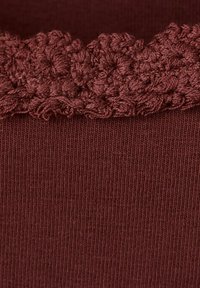 Tissu tricoté rouge foncé avec une bordure en dentelle texturée et festonnée le long du bord supérieur.
