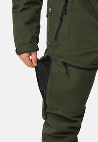 Zielone spodnie outdoorowe z zamykanymi kieszeniami i siateczkowym wykończeniem z boku dla wentylacji, wykonane z trwałego, wodoodpornego materiału.