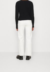 Czarny dziergany sweter o prążkowanej fakturze, zestawiony z białymi, szerokimi spodniami i masywnymi czarnymi butami, widziany od tyłu.