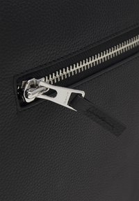 Mustapintainen nahkainen laukku, jossa on hopeinen vetoketju ja musta nahkainen nyöri, esittelee tyylikkään ja minimalistisen muotoilun.