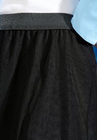 Haut blanc rentré dans une jupe noire texturée taille haute avec une large ceinture scintillante et une vue partielle d'une manche bleue sur le côté droit.
