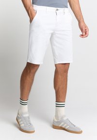 Witte katoenen shorts met voorzakken, iets boven de knie lengte, gecombineerd met grijze sneakers en gestreepte sokken.