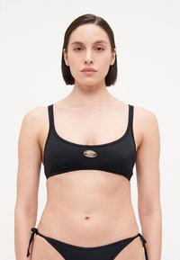 Svart bikinitopp med justerbare stropper, med en sølv oval detalj i midten. Glatt stoff med et minimalistisk design.