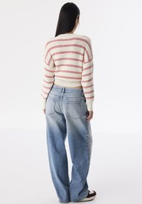 Pull crème cropped avec des rayures rouges, associé à un jean en denim clair ample avec un effet délavé et deux poches arrière.