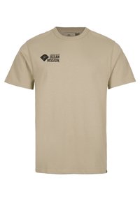 Camiseta de manga corta beige con el texto "ÚNETE A NUESTRA MISIÓN OCEÁNICA" y un pequeño logo negro en el lado izquierdo del pecho.
