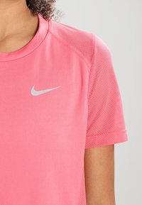 Rosa träningströja med kort ärm, med en mjuk tyg och meshdetaljer på axlarna; innehåller en silverfärgad Nike-logga.