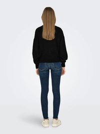 Sweater preto de malha com corte solto, combinado com jeans skinnies azul-escuro com bainha desfiada e ténis brancos de plataforma.