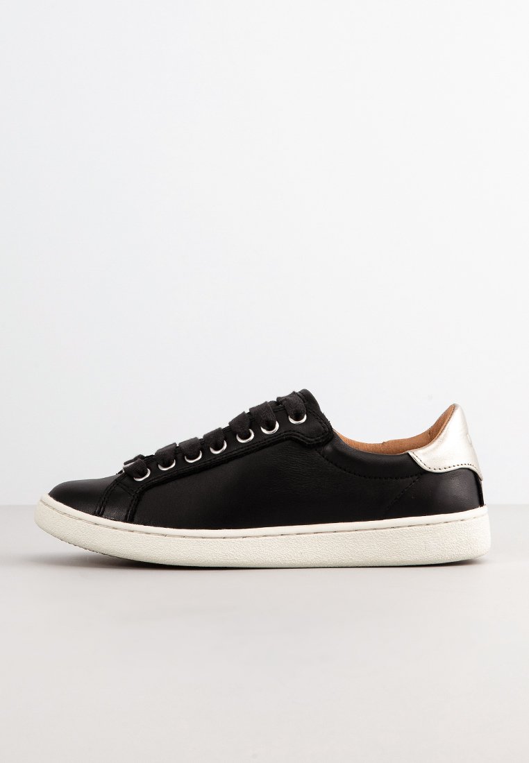 Zapatilla de cuero negra con diseño de tipo bajo, detalles plateados en el talón, suela de goma blanca y seis ojales para los cordones.