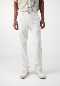 White cotton trousers with a straight-leg fit, featuring a button closure, side pockets, and minimal stitching details, paired with white sneakers.