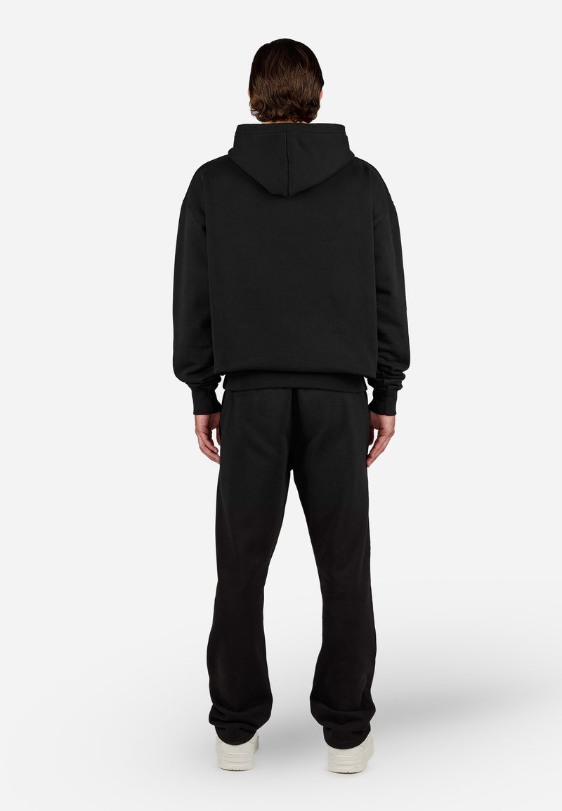Conjunto de sudadera con pantalones de chándal negros, con un corte relajado, color sólido, puños acanalados y capucha, sin patrones ni gráficos visibles.