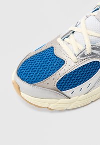 Αθλητικό παπούτσι με μπλε δίχτυ και ασημί συνθετικές λεπτομέρειες. Διαθέτει υφές υλικών, εκρού κορδόνια και μαλακή σόλα.