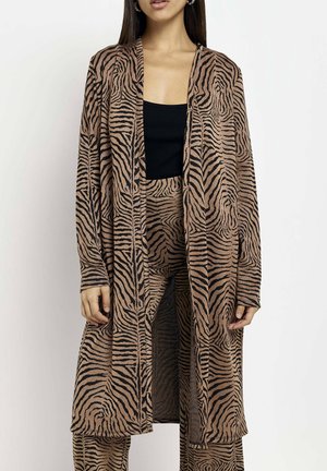 Woman wearing a brown and black tiger-striped long cardigan and matching pants over a black top, standing against a white background.