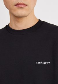 Black sweatshirt with a ribbed neckline and embroidered white "carhartt" logo on the chest. Smooth fabric texture, casual design.