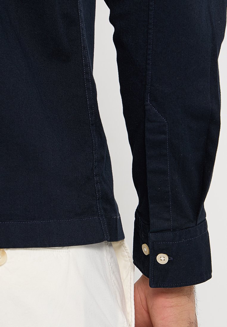 Marineblauwe langwerpige blouse met een aansluitend ontwerp, voorzien van knoopmanchetten, getailleerde naden en een gladde katoenstof textuur.