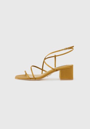 Yellow faux suede block-heeled sandals featuring thin crisscross straps and a square toe design. Smooth texture with a minimalistic style.