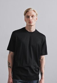 Svart t-skjorte med kort erme laget av glatt stoff, med diskrete flekkete mønstre og en klassisk Rund hals.