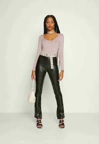 Blusa de manga longa em mauve com decote em forma de barco, combinada com calças justas pretas em couro sintético e um cinto a condizer. Os acessórios incluem uma pequena bolsa creme.