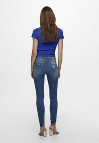 Blå randig kortärmad topp i kombination med åtsittande mid-rise blå jeans med målfärgsprutdetaljer, kompletterat med beige klacksandaler.