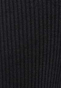 Zbliżenie na czarną, prążkowaną dzianinę, ukazującą pionowy wzór fakturowanego ściegu.