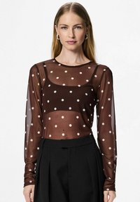Top trasparente marrone a maniche lunghe con pois bianchi, caratterizzato da un collo rotondo e un design aderente, abbinato a pantaloni neri a vita alta.