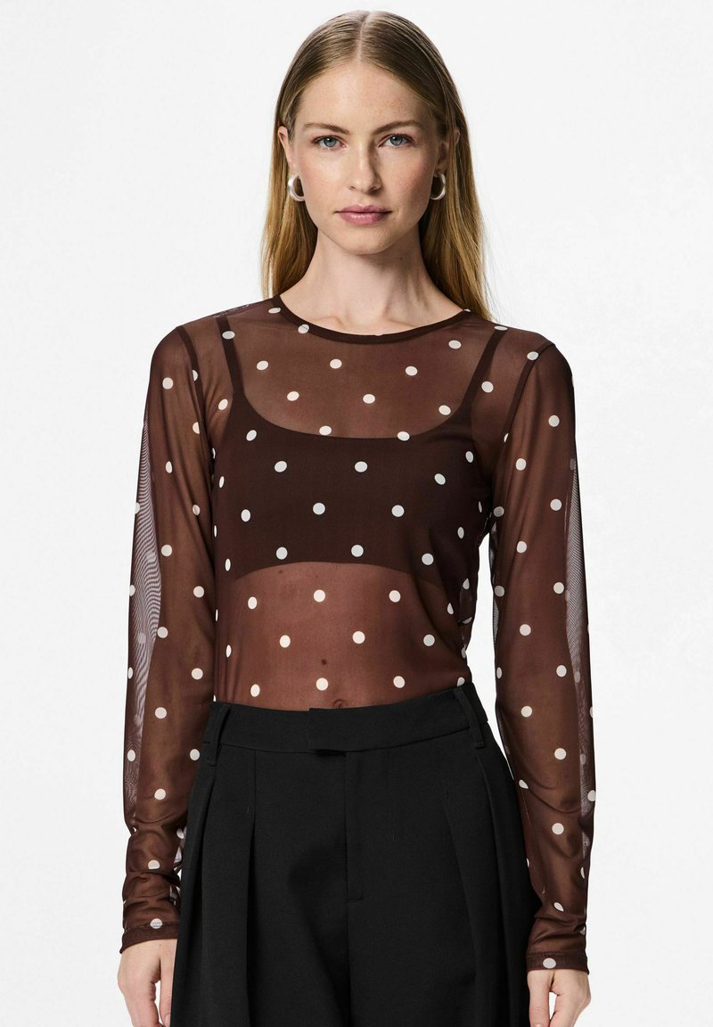 Top trasparente marrone a maniche lunghe con pois bianchi, caratterizzato da un collo rotondo e un design aderente, abbinato a pantaloni neri a vita alta.