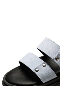 Tvåremmade sandaler med överdel i ljusblå mocka och svart texturerad sula. Har silverfärgade detaljer på remmarna.